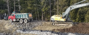 Photo of heavy machinery between a treeline and a barrier of large rocks